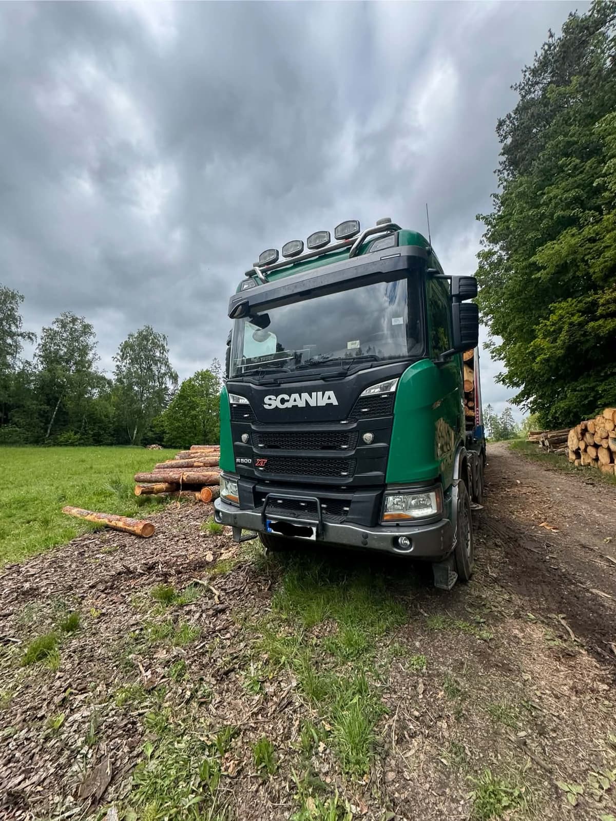 Skládka dřeva u lesní cesty a Scania R500 XT